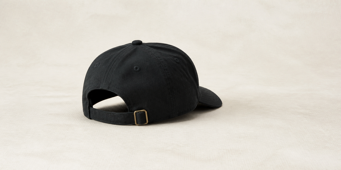 Rear view of a black dad hat with an adjustable brass buckle strap